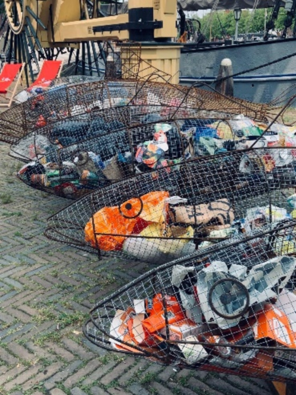 Afvalharingen - van zwerfvuil tot kunst - Op de foto zie je verschillende afvalharingen die gemaakt zijn van metaal gevuld met zwerfafval. De haring staan naast het Infopunt van VlaardingenDoen op de Westhavekade.